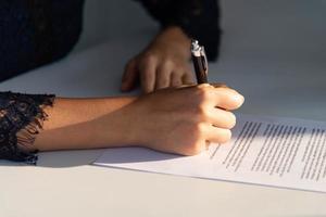 närbild kvinna hand skriver på vitt papper anteckning på det vita bordet på kontoret foto