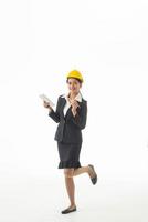 ung ingenjör kvinna bär svart kostym och gul skyddshjälm hålla anteckning eller tablett på isolerade vit bakgrund. foto