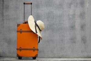 orange vintage resväska med sommarhatt på grå bakgrund med kopia utrymme för resor eller semester koncept foto