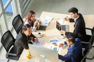 ovanifrån av grupp av multietniska upptagna människor som arbetar på ett kontor, flygfoto med affärsman och affärskvinna som sitter runt ett konferensbord med kopia utrymme, affärsmöteskoncept. foto