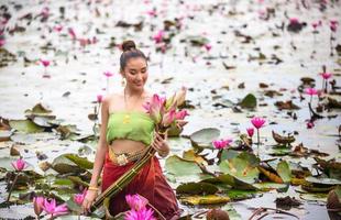 unga asiatiska kvinnor i traditionell klädsel i båten och rosa lotusblommor i dammen. vackra flickor i traditionell kostym. thailändsk flicka i retro thaiklänning, thailändsk flicka i traditionell dräkt foto