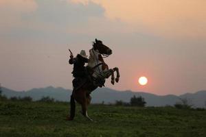 siluett cowboy på hästryggen mot en vacker solnedgång, cowboy och häst vid första ljuset, berg, flod och livsstil med naturligt ljus bakgrund foto
