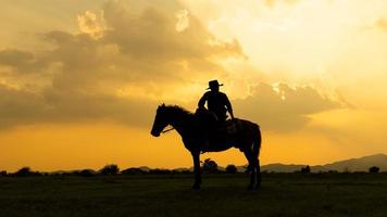 siluett cowboy på hästryggen mot en vacker solnedgång, cowboy och häst vid första ljuset, berg, flod och livsstil med naturligt ljus bakgrund foto