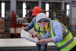 män industriingenjör som bär skyddshjälm när de står i en tung industrifabrik. underhållet av att arbeta på industriella maskiner och kontrollera säkerhetssystemets installation i fabriken. foto