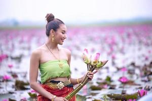 unga asiatiska kvinnor i traditionell klädsel i båten och rosa lotusblommor i dammen. vackra flickor i traditionell kostym. thailändsk flicka i retro thaiklänning, thailändsk flicka i traditionell dräkt foto