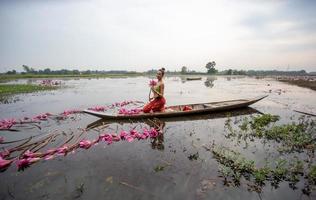 unga asiatiska kvinnor i traditionell klädsel i båten och rosa lotusblommor i dammen. vackra flickor i traditionell kostym. thailändsk flicka i retro thaiklänning, thailändsk flicka i traditionell dräkt foto