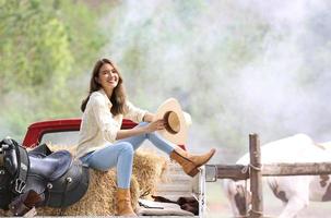 cowgirl modell poserar på gården. ett porträtt av en vacker ung cowgirl lutad mot en vägg i ett stall på gården. foto