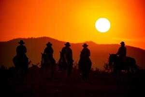 siluett cowboy på hästryggen mot en vacker solnedgång, cowboy och häst vid första ljuset, berg, flod och livsstil med naturligt ljus bakgrund foto