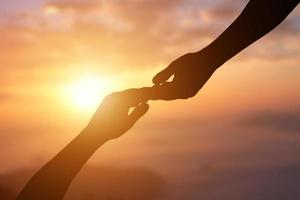 siluett av att ge en hjälpande hand, hoppas och stödja varandra över solnedgångsbakgrund. foto