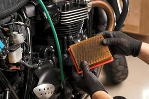 mekaniker håller smutsigt motorluftfilter över motorcykeln, arbetar i motorcykelgarage. reparationsservice och underhållskoncept foto