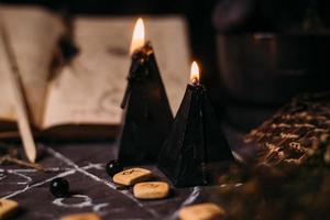 öppna gammal bok med magiska trollformler, runor, svarta ljus på häxbordet. ockult, esoteriskt, spådomskoncept och wicca-koncept. foto