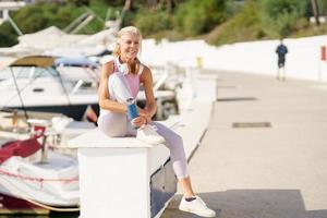 mogen idrottskvinna i fitness kläder dricksvatten från en metall fitness flaska utomhus. foto