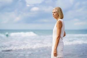 mogen kvinna stirrar lugnt på havet. äldre kvinna stående på en plats vid havet foto