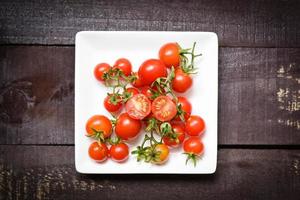 färska tomater på vit platta med trä mörk bakgrund ovanifrån foto