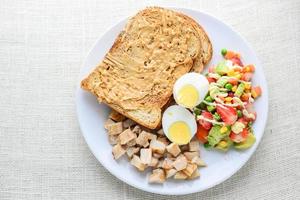 modern stil ren mat, jordnötssmör med bröd, kokt ägg, grillad kyckling och avokado, jordgubbar, grönsakssallad foto