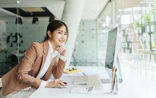 glad attraktiv asiatisk affärskvinna som arbetar med en bärbar dator och finansiellt dokument på kontoret, framgångsrika åtgärder, affärsidé. foto