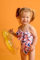 en liten flicka klädd i baddräkt vid ett och ett halvt års ålder hoppar eller dansar. flickan är väldigt glad. bild tagen i studion på en gul bakgrund. foto