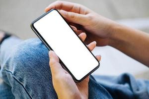 en kvinna som håller en mobiltelefon med en tom vit skärm. det tomma utrymmet på den vita skärmen kan användas för att skriva ett meddelande eller placera en bild. foto