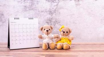 par nallebjörn med kalender på bord i trä. alla hjärtans dag firande foto