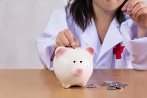 asiatisk flicka spelar som läkare balansera pengar i spargris foto