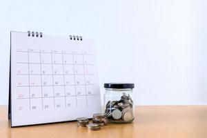 kalender med dagar och mynt i burken på träbord foto
