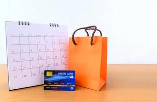 kalender med dagar och kreditkort och orange papperspåse på träbord. shopping koncept foto