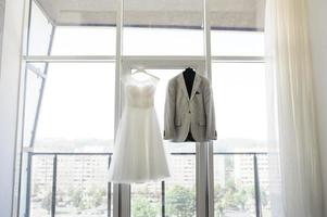brudgummens jacka och bröllopsklänning i bakgrunden av ett stort fönster. foto