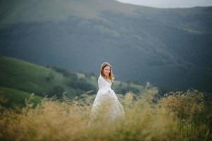 kvinna i en bröllopsklänning springer över fältet mot bergen foto