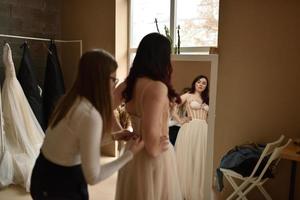 butiksägare som hjälper kvinna att prova klänningar i boutique foto
