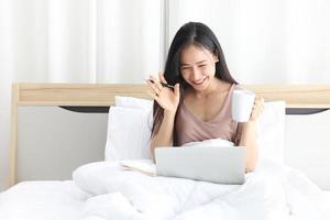asiatisk kvinna som arbetar online hemifrån med laptop på sin säng för ett nytt normalt liv under karantänperioden från covid-19 foto