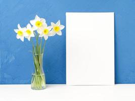 bukett färska blommor, tomt vitt papper på vitt bord, mittemot blå texturerad betongvägg foto