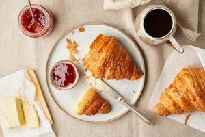 två läckra croissanter och varm dryck i mugg. morgon fransk frukost foto