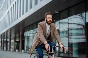 ung hipster affärsman kommer att arbeta på cykel. miljövänligt transportkoncept foto