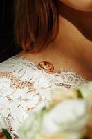 ett par vigselringar av bruden och brudgummen på axeln av den framtida frun i en vit klänning. bröllopstillbehör, ceremoni, smycken, brudbukett med rosa rosor. utrymme för text foto
