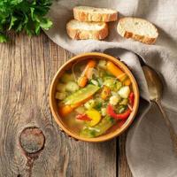ljus vår grönsakskost vegetarisk soppa. ovanifrån, brun rustik träbakgrund, linneservett. foto