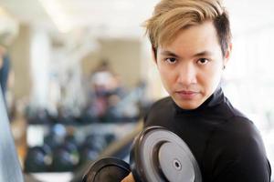 asiatisk stilig ung man gör ett viktpass genom att använda hantel i gymmet. foto