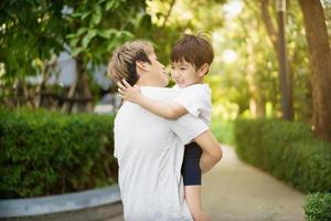 glad asiatisk liten pojke tycker om att spela och gå i parken med pappa på nära håll, asiatisk pojke har ett vackert leende medan han tittar på sin far. liten pojke porträtt på parken och lekplatsen. foto
