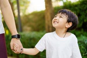 glad asiatisk liten pojke tycker om att spela och gå i parken med pappa på nära håll, asiatisk pojke har ett vackert leende medan han tittar på sin far. liten pojke porträtt på parken och lekplatsen. foto