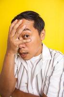 närbild av stilig asiatisk man som täcker hans ansikte med händerna isolerade på gul bakgrund foto