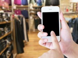 kvinna hand håller smart telefon, surfplatta, mobiltelefon på oskärpa kläder butik bakgrund foto