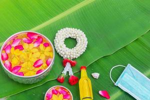 songkran festival bakgrund med jasmin girland blommor i en skål med vatten, parfym och kalksten på en grön våt banan blad bakgrund. foto