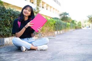 student ung flicka med rosa ryggsäck sitter vid foten med skolbakgrund. foto