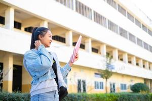 leende flicka hålla rosa bok stående på bygga bakgrund, tillbaka till skolan. foto