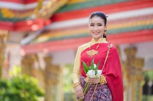 attraktiv thailändsk kvinna i en gammal thailändsk klänning håller färska blommor och hyllar Buddha för att önska sig den traditionella songkran-festivalen i thailand foto