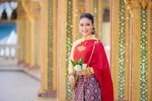 attraktiv thailändsk kvinna i en gammal thailändsk klänning håller färska blommor och hyllar Buddha för att önska sig den traditionella songkran-festivalen i thailand foto