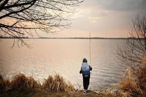 pojke i hoodie vid sjön med en vass i händerna. foto