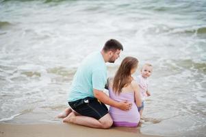 sommarsemester. föräldrar och människor utomhusaktiviteter med barn. trevlig familjesemester. far, gravid mor, baby dotter på havet sandstrand. foto