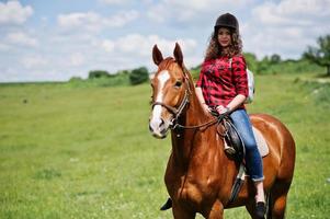 ung söt flicka rider en häst på ett fält på solig dag. foto