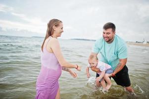 sommarsemester. föräldrar och människor utomhusaktiviteter med barn. trevlig familjesemester. far, gravid mor, baby dotter på havet sandstrand. foto