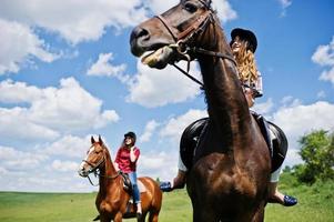 dra unga vackra flickor som rider en häst på ett fält på solig dag foto